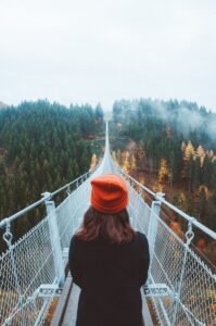 woman wearing knit cap walking on white bridge between trees during daytime